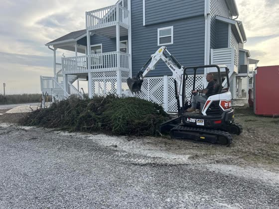 Mini excavator clearing brush beside a home