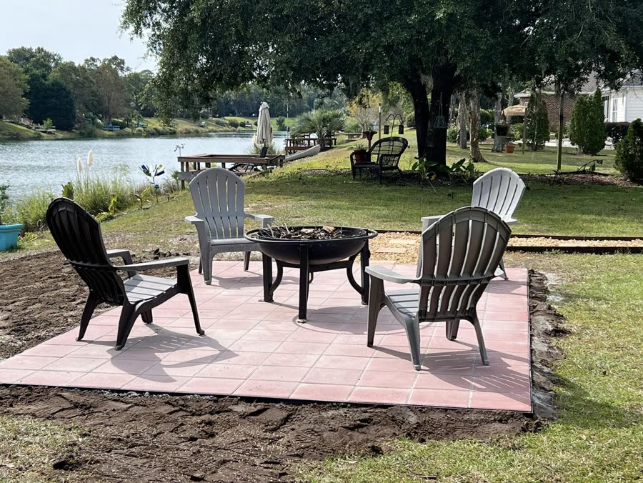 Paver patio with a fire pit and chairs beside a lake
