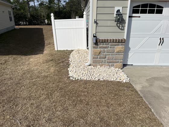 White rock border along a garage and vinyl fence